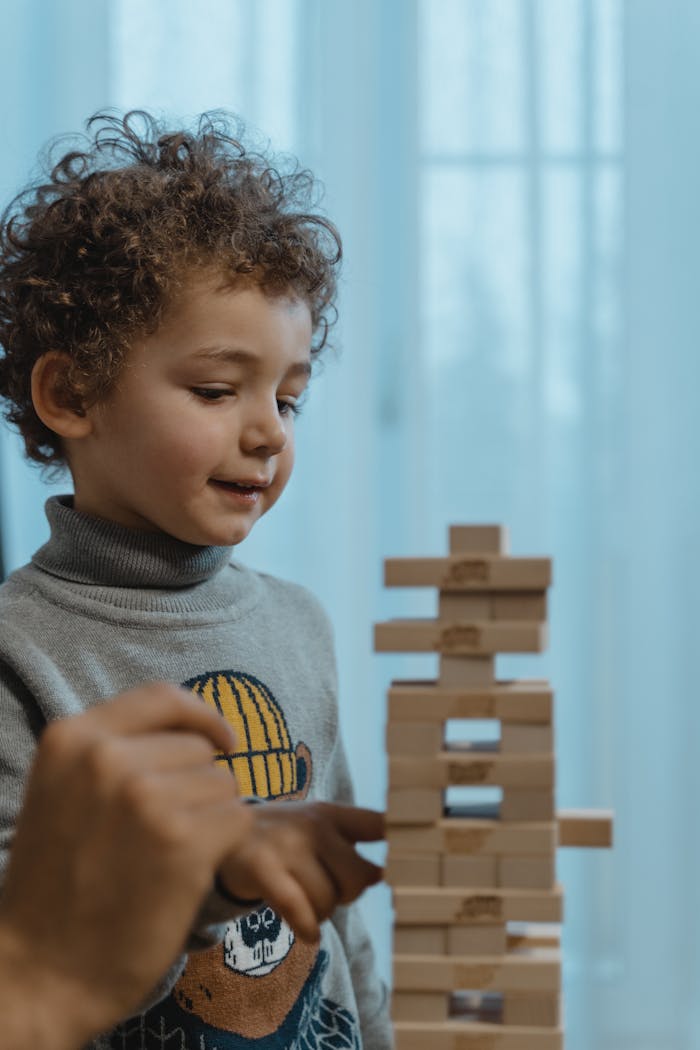 gallery-4 A young boy plays with wooden blocks, guided by an adult hand indoors.