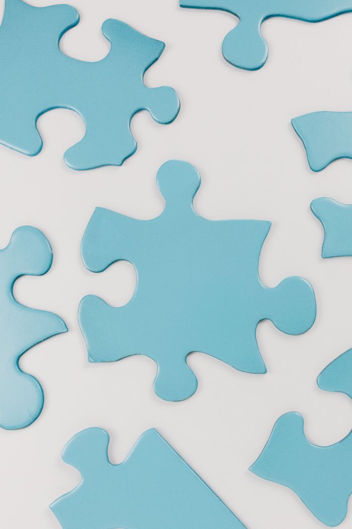 about-02 Close-up of blue puzzle pieces scattered on a white surface, conceptual and minimalistic.