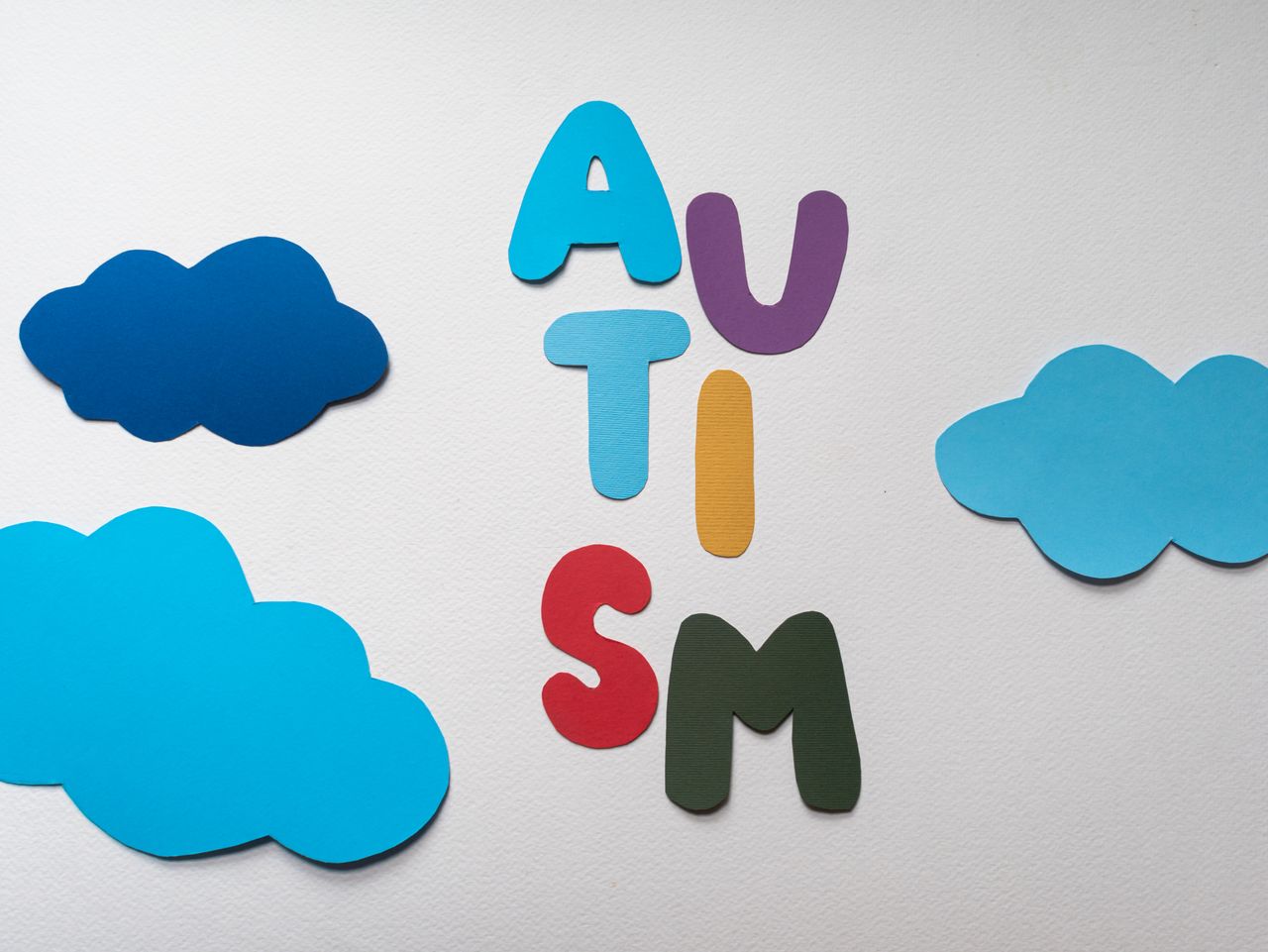 services-01 Vibrant letters spelling 'AUTISM' surrounded by blue paper clouds on a white background.